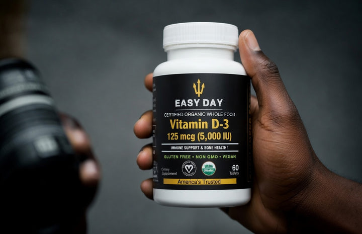 Hand holding a bottle of Easy Day Vitamin D-3 supplement against a dark background